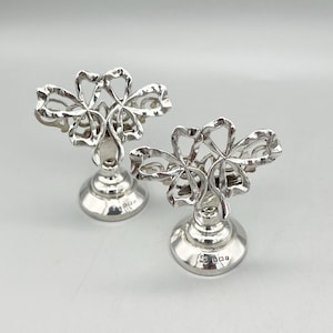 May include: A pair of silver napkin rings with a floral design. The rings are made of sterling silver and have a hallmarked base.