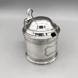 May include: Silver sugar or honey pot with a lid and a handle. The pot has an engraved design around the top and bottom.