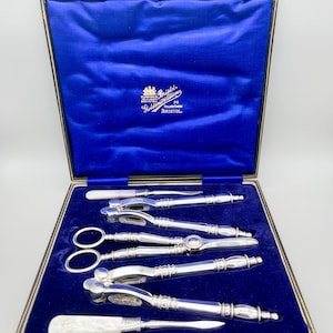 Op de afbeelding: Een vintage verzilverde serveerset, inclusief notenkrakers, schaar en een mes, gepresenteerd in een blauwe fluwelen doos. De doos is voorzien van de tekst "Bristol" en een wapen.