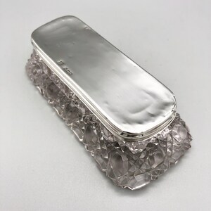 May include: A silver-plated rectangular box with a clear glass base. The glass base has a cut-glass design. The box has a hallmark on the bottom.