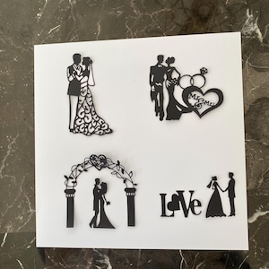 Puede incluir: Decoraciones de boda de silueta negra sobre un fondo blanco. Las decoraciones incluyen una novia y un novio, un corazón con anillos, un arco y la palabra "Love".