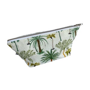 May include: A white zippered pouch with a palm tree print. The pouch is made of a soft, textured fabric and has a white zipper.