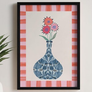 Könnte beinhalten: Gerahmter Kunstdruck mit einer blau gemusterten Vase, die drei bunte Blumen enthält. Der Druck hat einen rosa-orangefarbenen Streifenrand und einen schwarzen Rahmen. Das Kunstwerk wird an einer hellen Wand gezeigt.