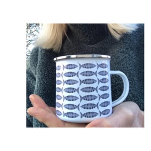 May include: White enamel mug with a pattern of blue fish. The mug has a silver rim and a handle.