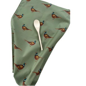 May include: A green tea towel with a repeating pattern of brown and green pheasants. A wooden spoon is lying on top of the towel.