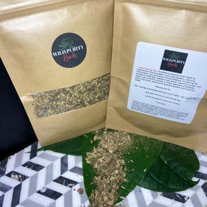 Puede incluir: Dos bolsas de papel marrón con una etiqueta blanca que dice "Wild Purity Herbs" y una descripción del "Herbal Revival Tea". El té es una mezcla de hierbas para apoyar la salud general. Las bolsas están llenas de hierbas secas y están sobre una hoja verde y una superficie de azulejos blancos y grises.