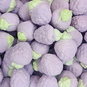 May include: A close-up of a pile of purple and green marshmallow sweets shaped like strawberries. The sweets are covered in a fine layer of sugar.