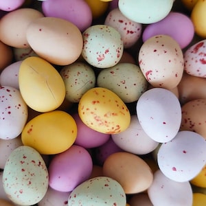 May include: A collection of pastel-coloured candy eggs with red and white speckles. The eggs are arranged in a random pattern.