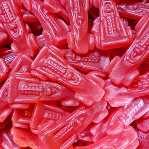 May include: A close-up of a pile of bright red candy shaped like race cars. The candy is glossy and has a smooth texture.