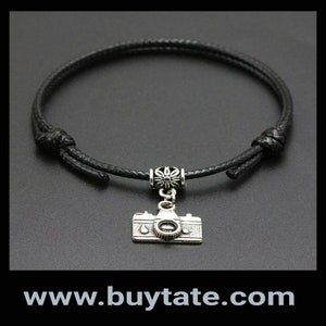 May include: A black adjustable cord bracelet with a silver camera charm and a silver flower bead.