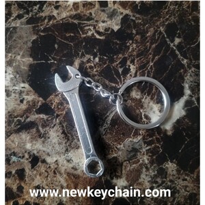 May include: Silver wrench keychain with a silver key ring. The wrench has a hexagonal head and a rounded handle. The keychain is attached to the ring with a silver chain. The text "www.newkeychain.com" is visible at the bottom of the image.