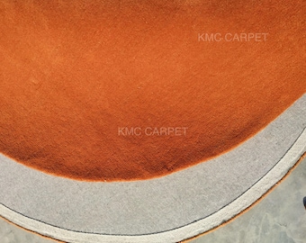 May include: Close-up of a section of a round, orange carpet. The carpet has a textured surface and a gray border. The text "KMC CARPET" is visible on the carpet.