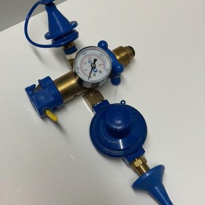 May include: A blue and brass gas regulator with a pressure gauge. The regulator has a circular gauge with a needle and numbers. The device has multiple blue and brass components, including a nozzle and a dial.