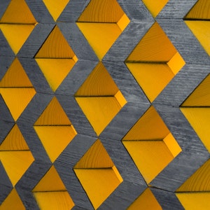 Puede incluir: Un patrón geométrico de triángulos de madera amarillos y negros. Los triángulos están dispuestos en un patrón repetitivo, creando una textura visualmente interesante.