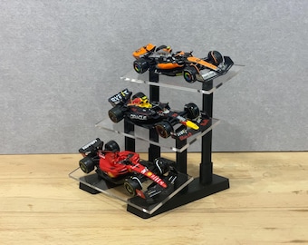 May include: A three-tiered acrylic display stand with three miniature Formula 1 race cars. The top car is orange and black with the word "Oracle" on the side. The middle car is black with red and yellow accents and the word "Oracle" on the side. The bottom car is red with black and white accents and the word "Repsol" on the side.