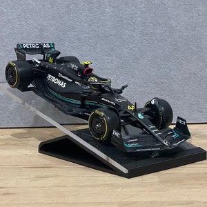 May include: A black and green Formula 1 race car model with the Petronas logo and the number 44 on the side. The car is on a black display stand.