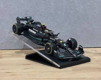 Può includere: Un modello di auto da corsa di Formula 1 nero e verde con il logo Petronas e il numero 44 sul lato. L'auto è su un espositore nero.