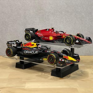 Könnte beinhalten: Zwei Formel-1-Rennwagen auf einem schwarzen Präsentationsständer. Das obere Auto ist rot mit der Nummer 55 und den Aufschriften "Oracle" und "Bybit". Das untere Auto ist schwarz mit den Aufschriften "Red Bull" und "Oracle".