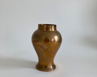 May include: A vintage brass vase with a wide, rounded body and a narrow, cylindrical neck. The vase has a warm, golden hue with subtle variations in color, and stands approximately 8 inches tall.