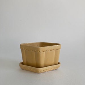 May include: A square ceramic planter with a scalloped rim and a matching saucer. The planter is a pale yellow color.
