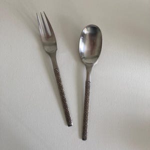 May include: A stainless steel fork and spoon set featuring a textured handle design with a repeating pattern of small circles and intersecting lines. Both utensils have a polished finish on the head and a matte, patterned handle.