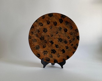 May include: A large, round ceramic plate with a brown and black leopard print design. The plate is on a black stand.