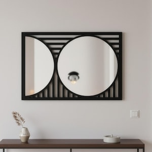 Może przedstawiać: Nowoczesne, geometryczne lustro ścienne z czarną ramą. Lustro ma dwie okrągłe powierzchnie odbijające i prostokątną ramę z paskami. Jest zamontowane na białej ścianie nad ciemnobrązowym stolikiem konsolowym.