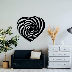 May include: Black and white heart-shaped wall art with a layered, optical illusion design. The artwork is mounted on a light gray wall, creating a striking contrast. The room features a black sofa, a white dresser, and a floor lamp.