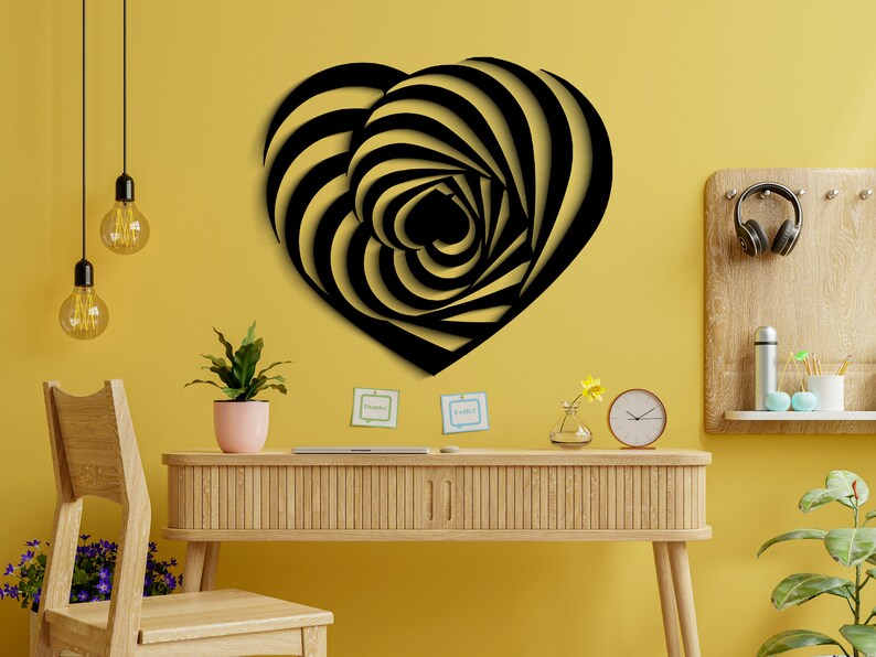 May include: Black and gold heart-shaped wall art with a spiral design. The artwork is mounted on a yellow wall above a wooden desk. The desk has a plant, clock, and other decorative items.