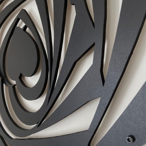 May include: Black metal wall art featuring a stylized design with a spiral and geometric shapes. The artwork has a matte finish and is mounted on a white wall. The design includes a spade shape.
