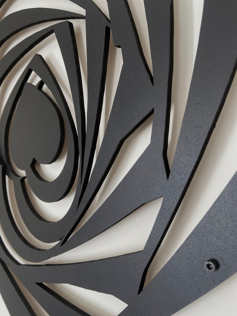 May include: Black metal wall art featuring a stylized design with a spiral and geometric shapes. The artwork has a matte finish and is mounted on a white wall. The design includes a spade shape.