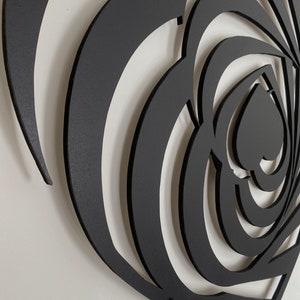 May include: Black metal wall art featuring a heart-shaped design with layered, swirling patterns. The artwork has a matte finish and is mounted on a white wall. The design incorporates multiple heart shapes within the larger form.