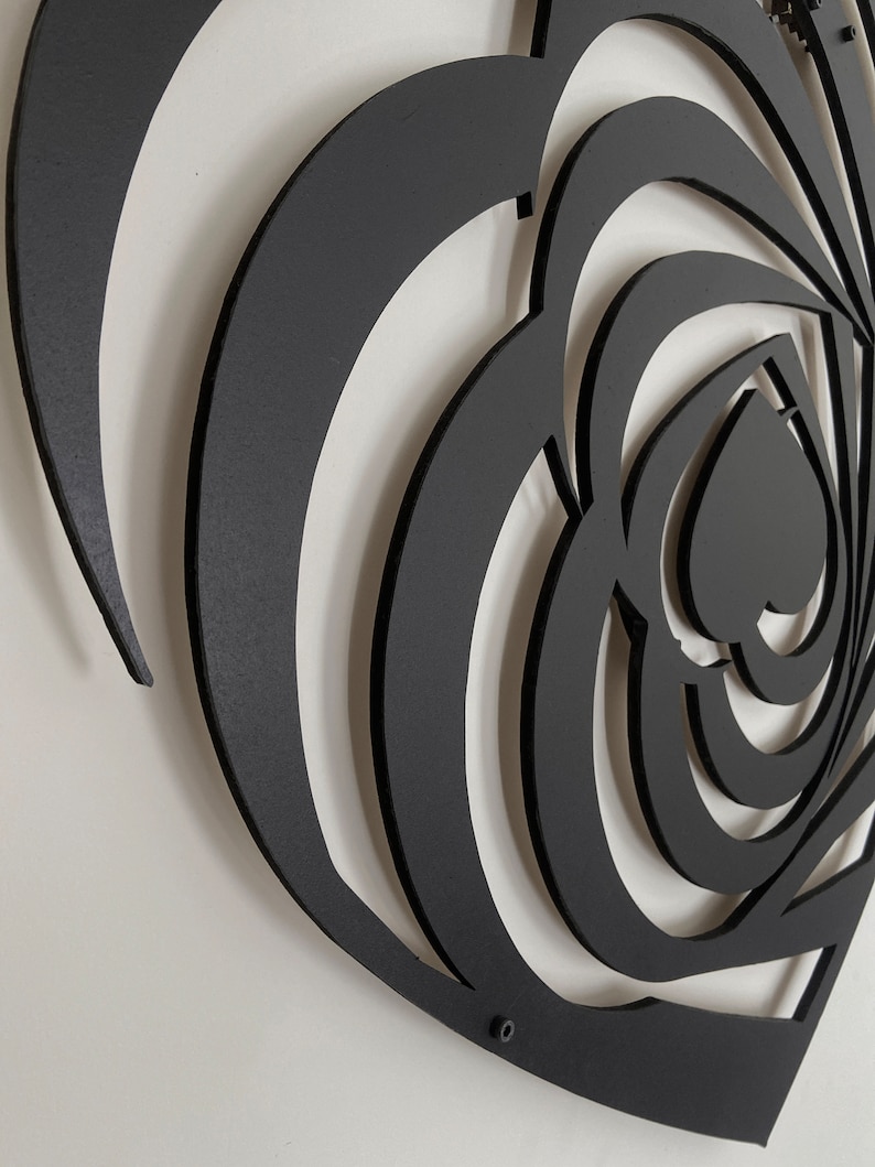 May include: Black metal wall art featuring a heart-shaped design with layered, swirling patterns. The artwork has a matte finish and is mounted on a white wall. The design incorporates multiple heart shapes within the larger form.