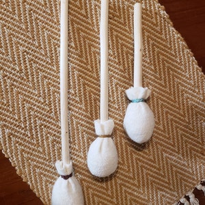 Peut inclure: Trois baguettes en bois avec des boules de tissu blanc attachées aux extrémités. Les boules de tissu sont attachées avec de la ficelle et ont un aspect rustique et fait main.