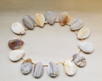 Puede incluir: Una hebra de 15 cuentas de madera petrificada en forma de lágrima en varios tonos de marrón, beige y blanco. Las cuentas están enhebradas en un alambre dorado.