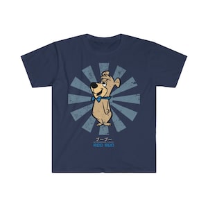 Pode incluir: Uma camiseta azul marinho com uma ilustração de estilo retro de um cão de desenho animado usando uma gravata borboleta azul. A ilustração é cercada por um padrão de raios de sol azul e branco. O texto "ルーファー" e "ROO ROO" é impresso abaixo da ilustração.