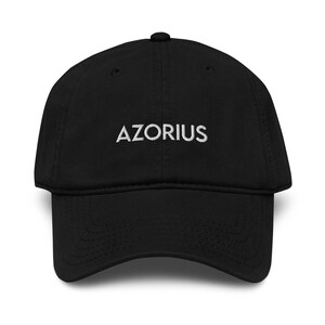 May include: A black baseball cap featuring the word "AZORIUS" embroidered in white. The cap has a curved peak and a rounded crown. A fashionable accessory for everyday wear.