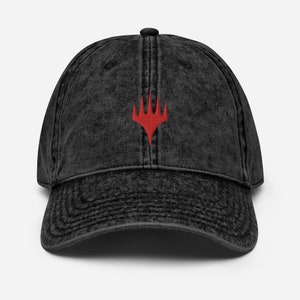 Könnte beinhalten: Eine schwarze, vintage gewaschene Baseballkappe aus Baumwolle mit einem roten, gestickten Magic: The Gathering-Symbol.