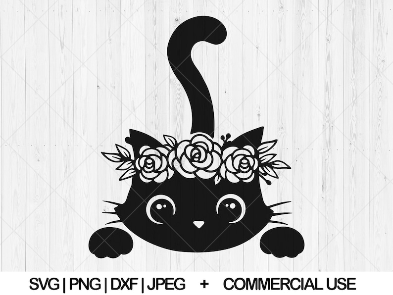 May include: Black cat with a floral crown peeking out from behind a white wooden surface. The cat has large eyes and a cute expression.