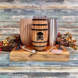 May include: Three wooden tumblers with a skull and crossbones design on one of the tumblers. The tumblers are sitting on a wooden tray with a wooden coaster.