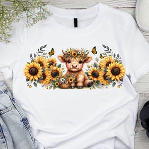 May include: White t-shirt with a cute cartoon illustration of a brown and white cow wearing a flower crown and surrounded by sunflowers.