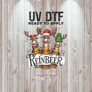 May include: A whimsical design featuring three beer bottles decorated as reindeer with antlers, Santa hats, and string lights. The text "ReinBEER" is displayed below the bottles, with "UV DTF READY TO APPLY" above.