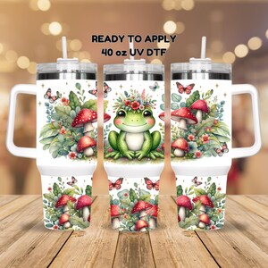 May include: Three 40 ounce stainless steel tumblers with lids and handles. The tumblers are decorated with a whimsical design of a frog wearing a flower crown, mushrooms, and butterflies. The text "READY TO APPLY 40 oz UV DTF" is printed on the top of the tumblers.