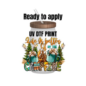 May include: White tumbler with a wood lid and a straw. The tumbler has a UV DTF print of a campfire scene with the text "Life is better by the campfire".