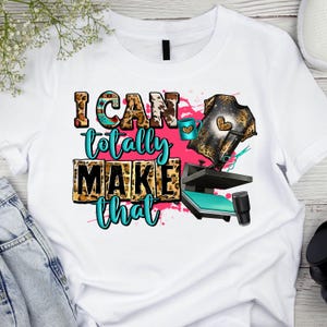 May include: White t-shirt with a graphic design that says "I can totally make that". The graphic includes a heat press, scissors, and a leopard print design.
