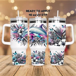 May include: Three 40 ounce stainless steel tumblers with a white background and colorful floral designs. The center tumbler features a blue and purple dolphin swimming through the flowers. The text "READY TO APPLY 40 oz UV DTF" is at the top of the image.
