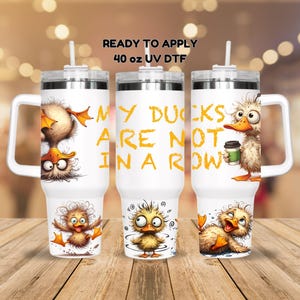 May include: Three white 40 ounce stainless steel tumblers with lids and straws. The tumblers feature a design of cartoon ducks with the text "My Ducks Are Not In A Row".