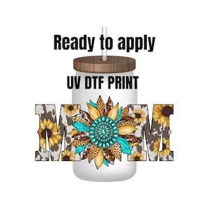 May include: A white tumbler with a brown wood lid and a straw. The tumbler has a UV DTF print of the word "MOM" with sunflowers and cowhide print. The text "Ready to apply" is above the tumbler.