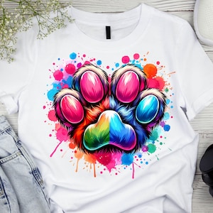May include: A white t-shirt with a colorful paw print design. The paw print is surrounded by colorful watercolor splatters.