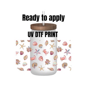 May include: A white tumbler with a wooden lid and a straw. The tumbler has a UV DTF print of seashells, starfish, and crabs. The text "Ready to apply" is above the tumbler and the text "UV DTF PRINT" is on the tumbler.